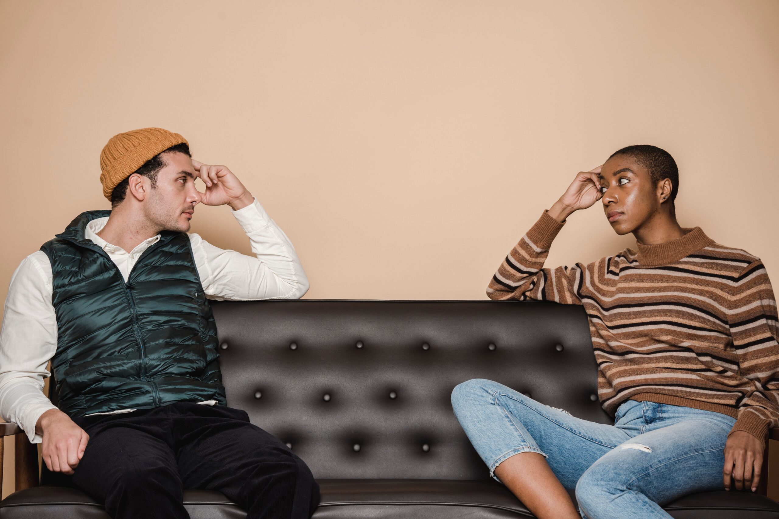 couple sitting on either end of a brown leather couch looking at each other curiously