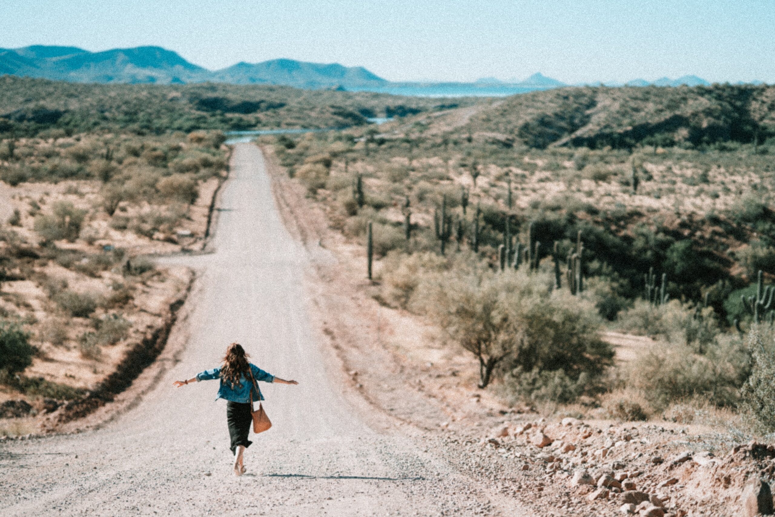 woman walking on a path in the desert with her arms stretched out.