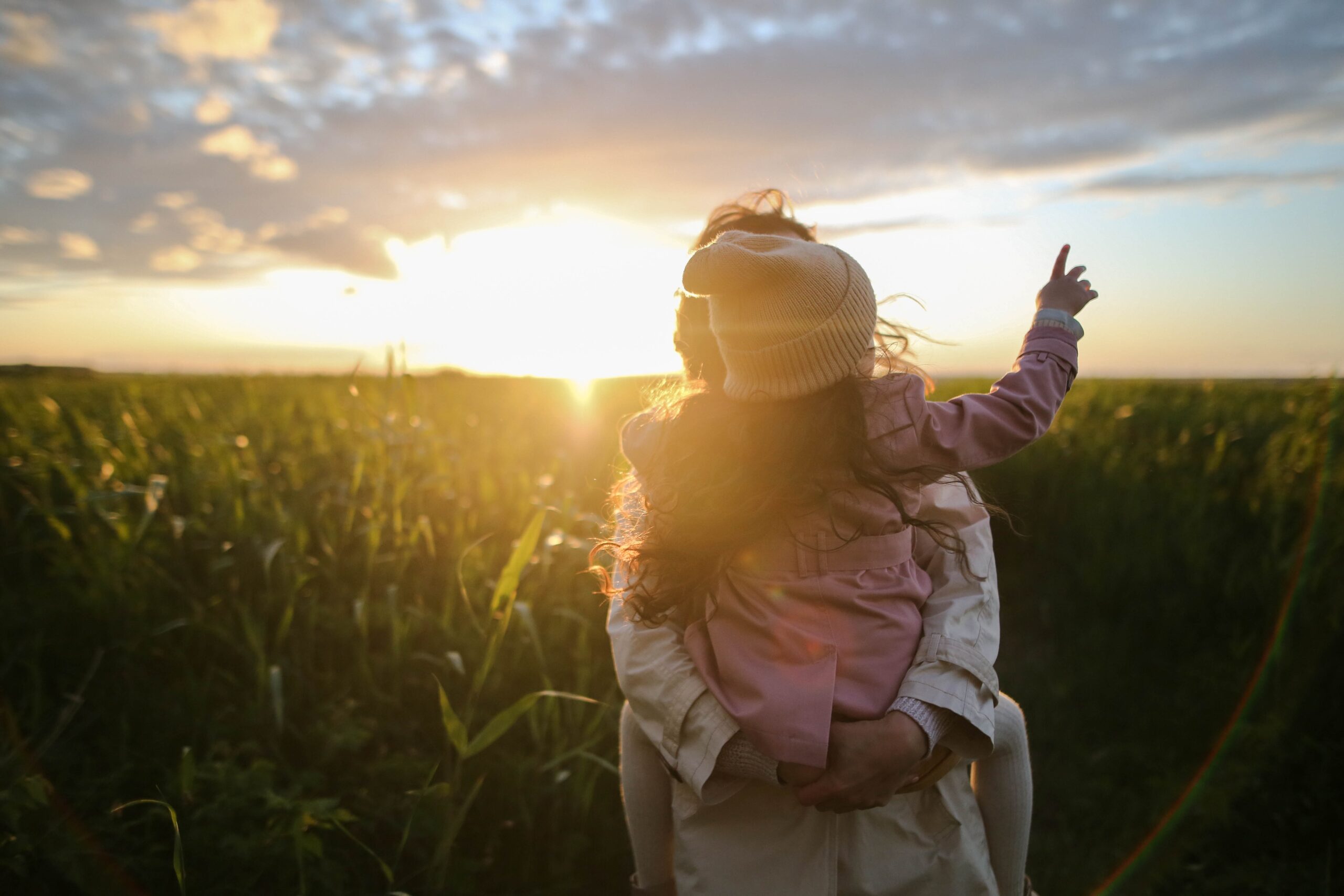 mother and child standing in a field at sunset