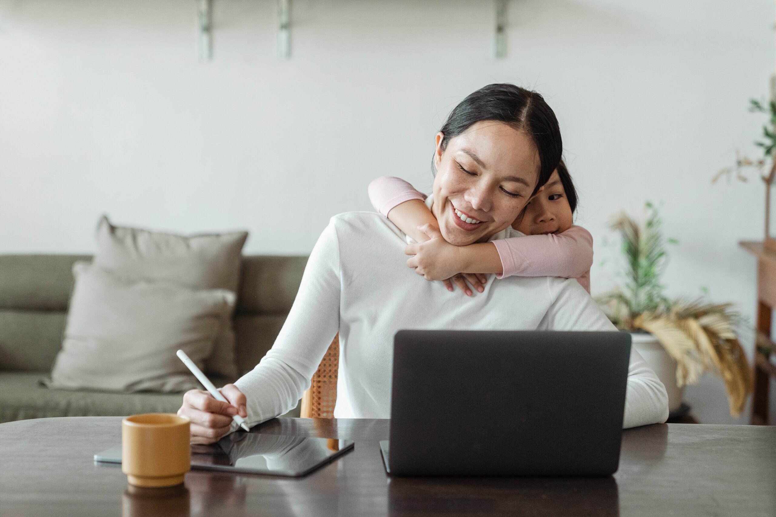 woman at her computer with a child draped over her back