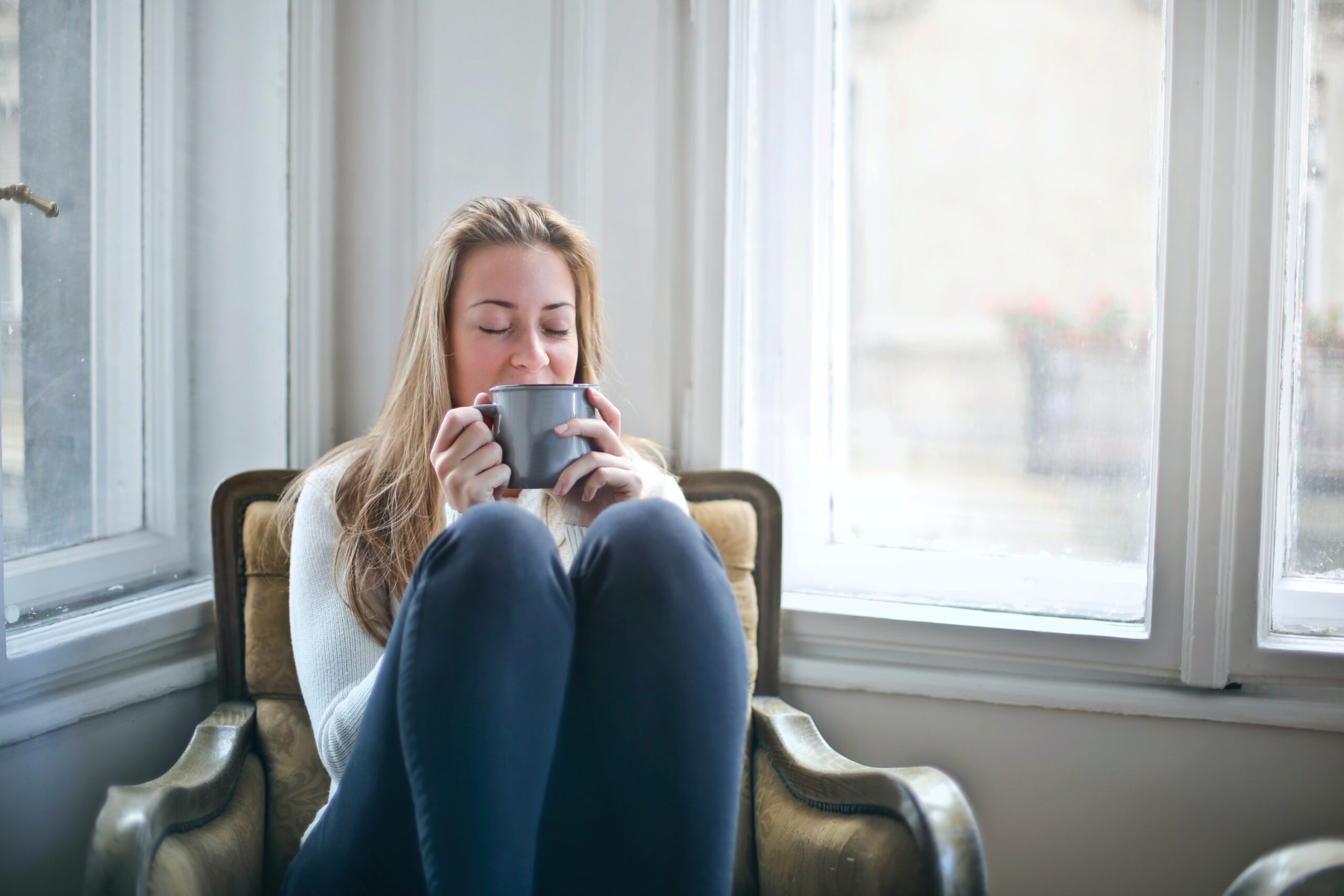 woman sitting next to a window sipping tea