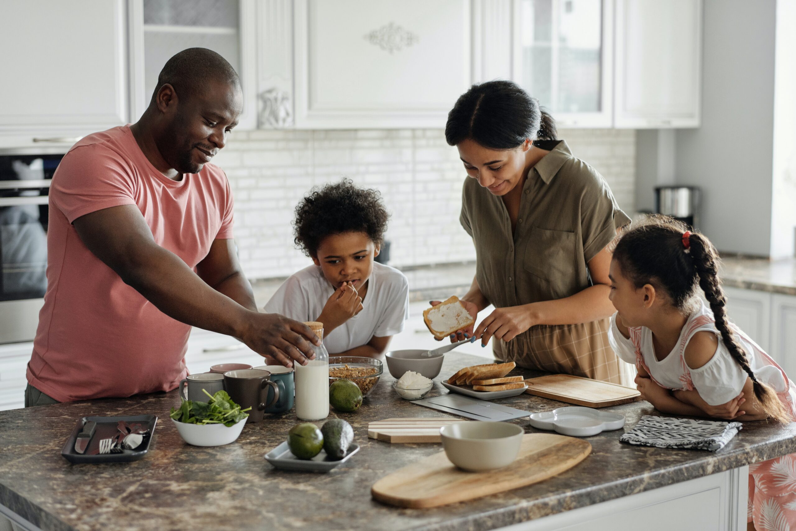 mother, father and two daughters gathered around a kitchen island making food.