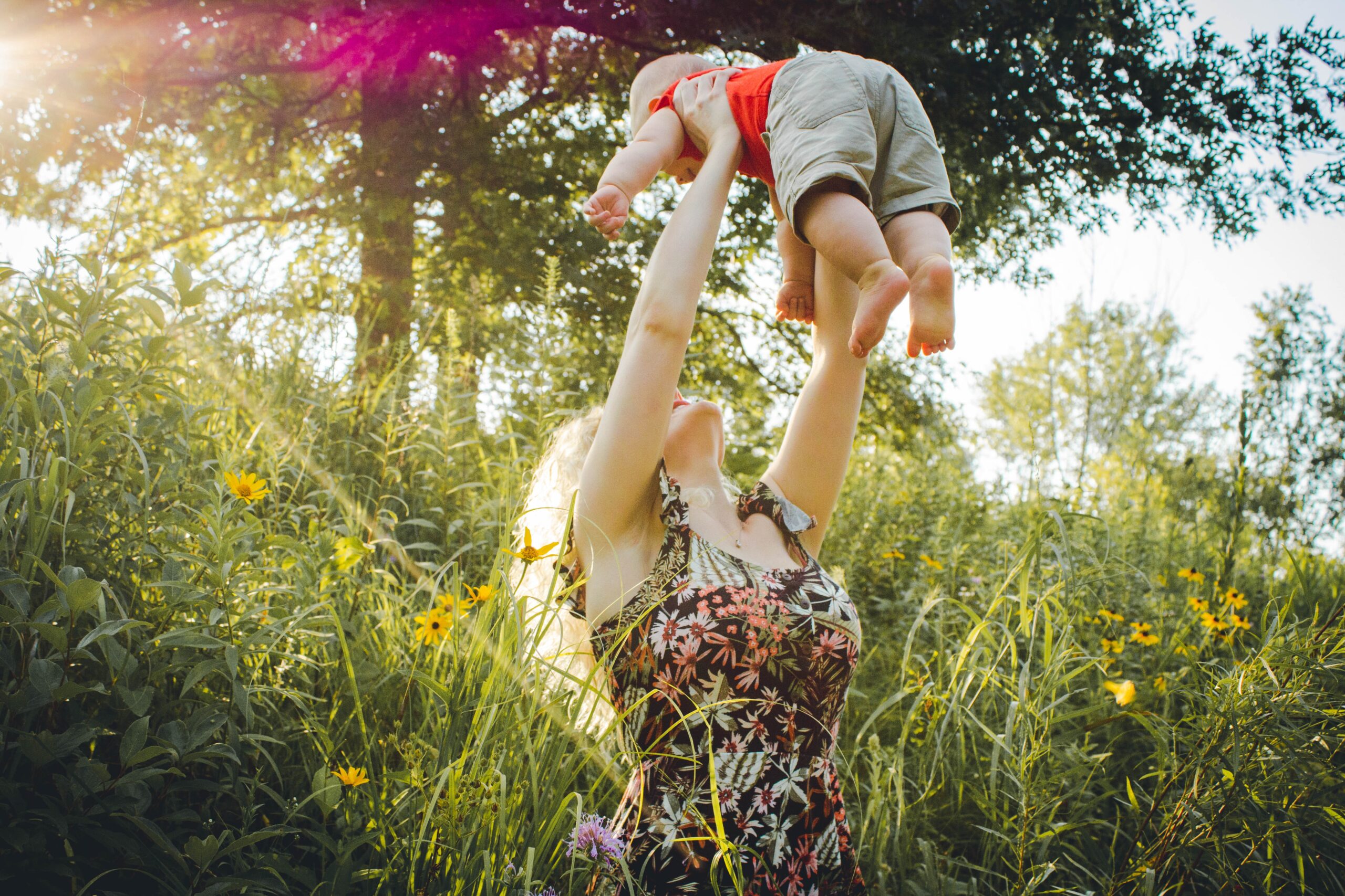 mother tossing child into the air in a field