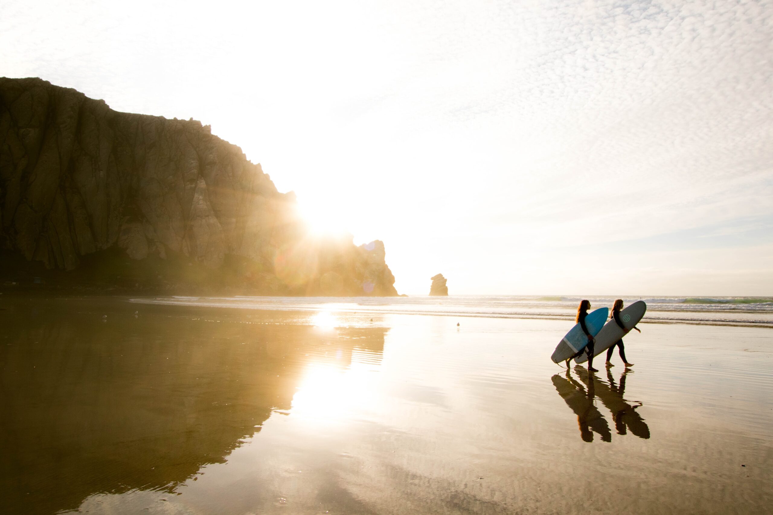 two people carrying surfboards walking a California beach