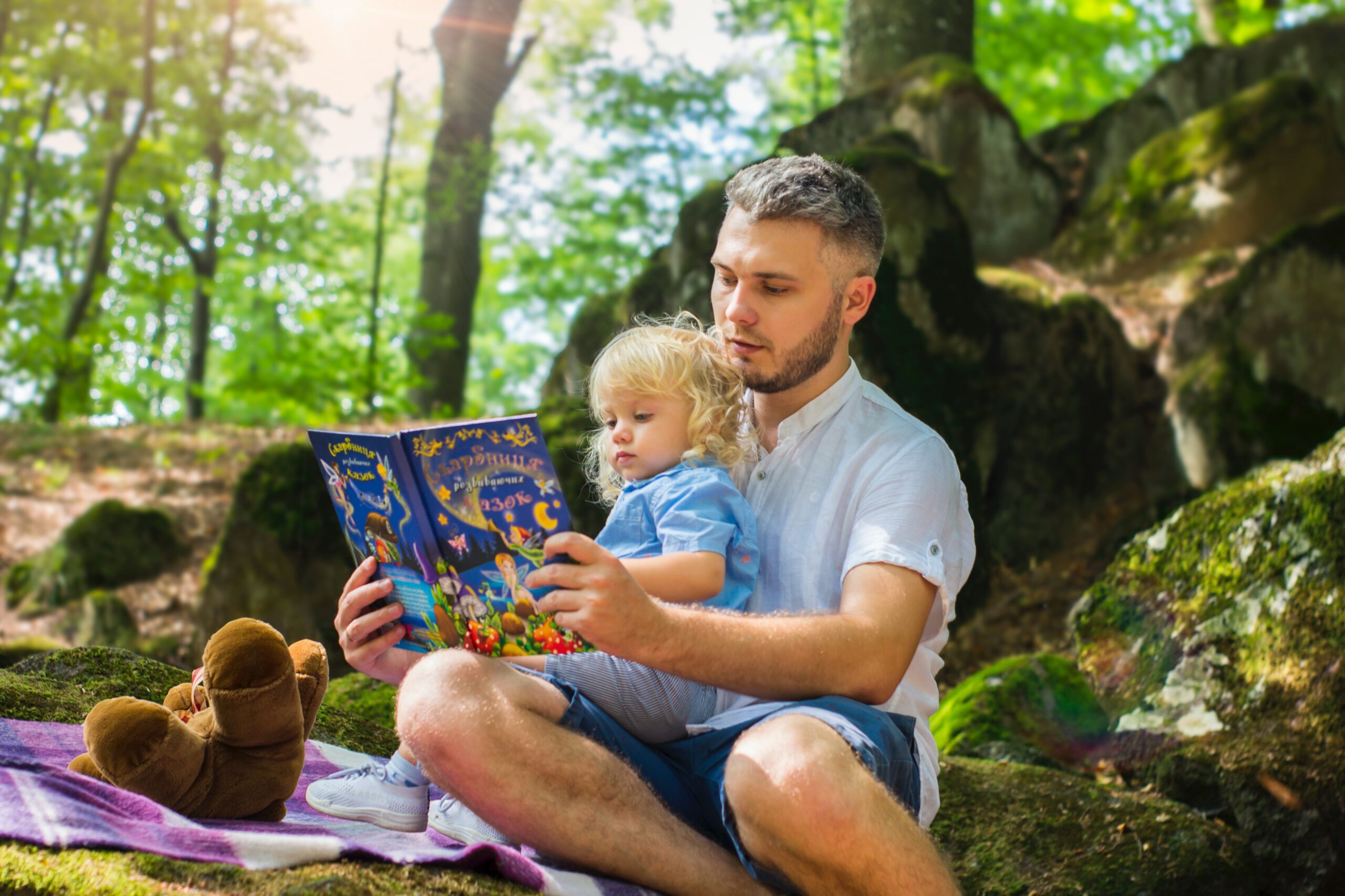 man with book reading to child in his lap outdoors