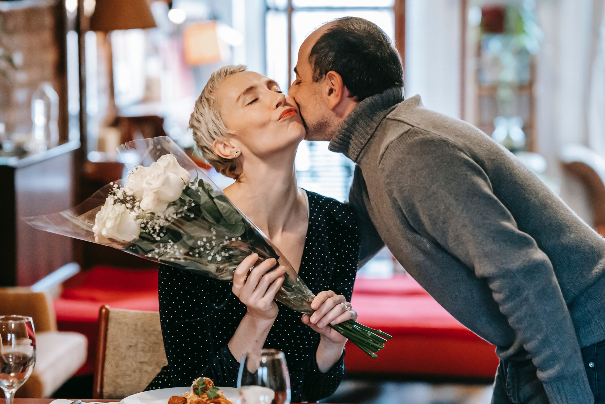 man kissing a woman holding flowers in a restaurant