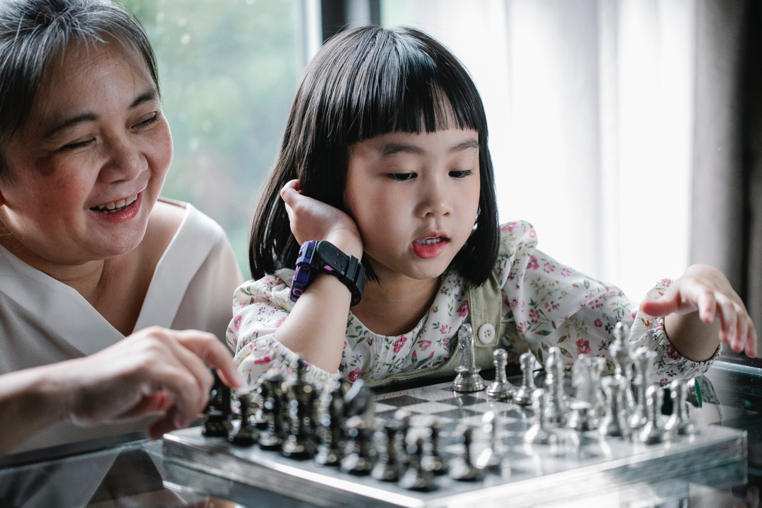 asian grandmother playing chess with granddaughter
