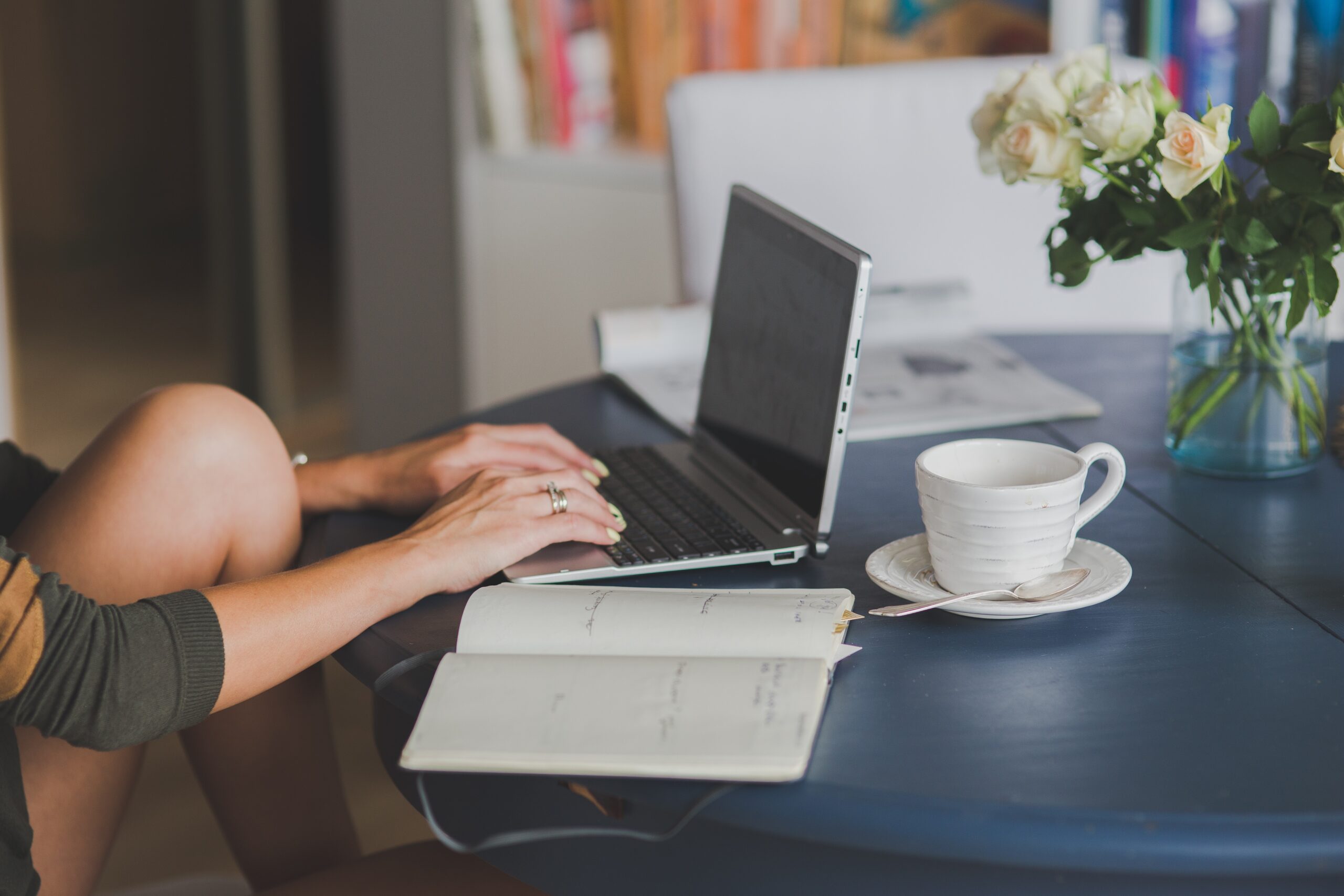 person sitting at table typing on a laptop with coffee and a notepad next to them