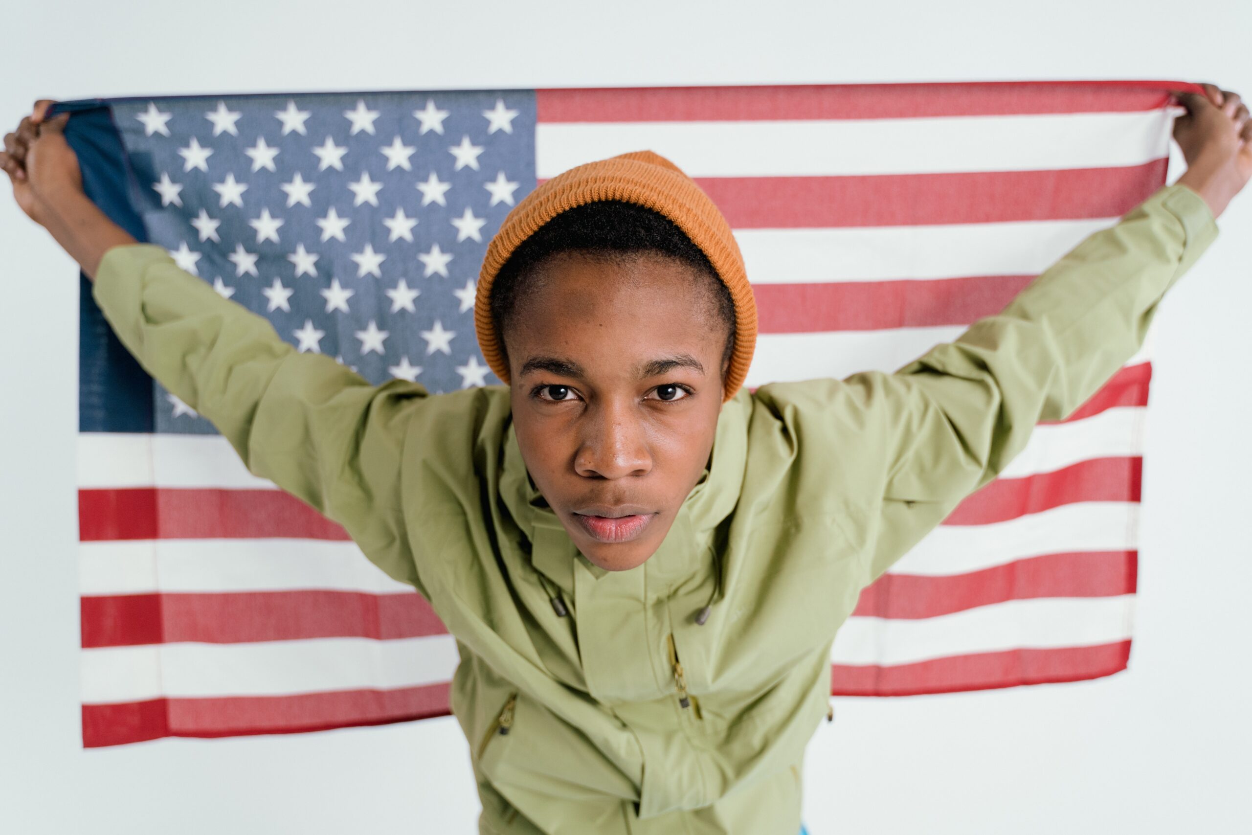 black man in orange hat holding US flag behind him