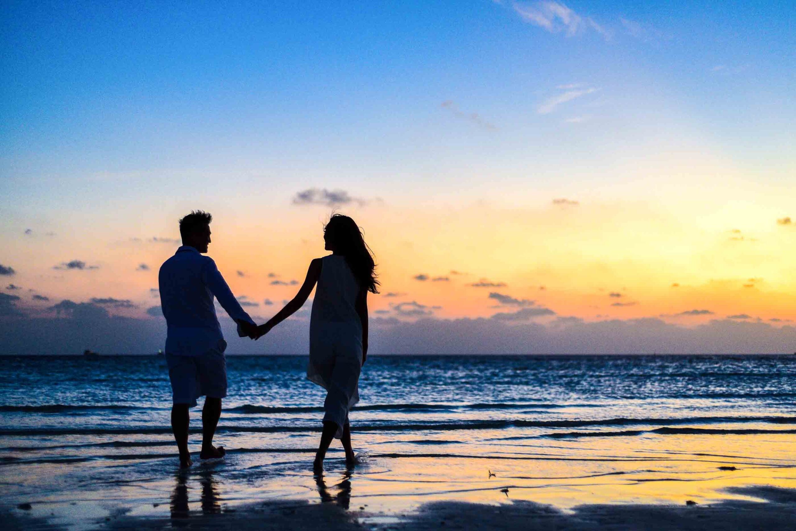 man and woman holding hands walking on beach at sunrise