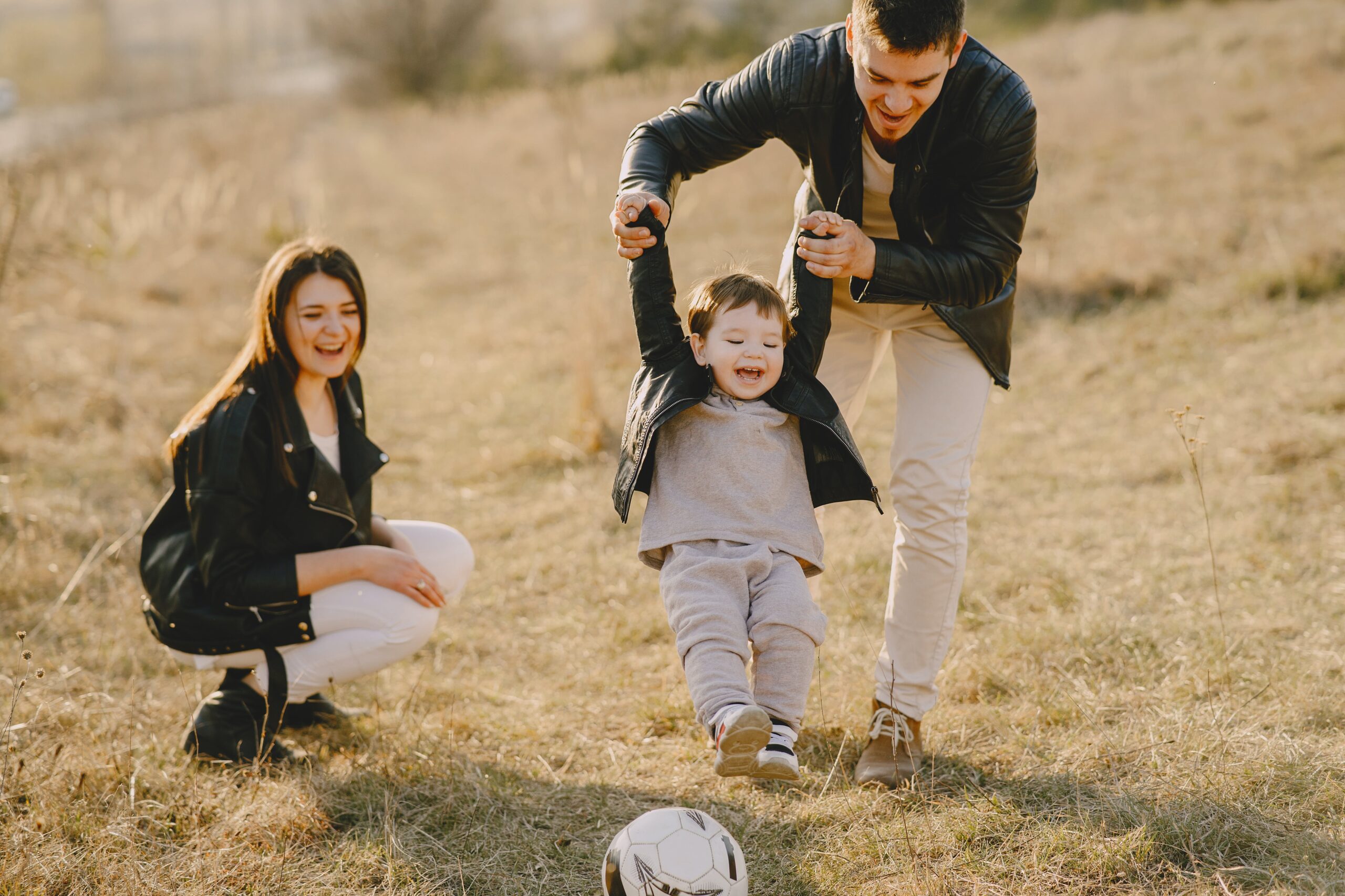 parents with small child playing soccer outside