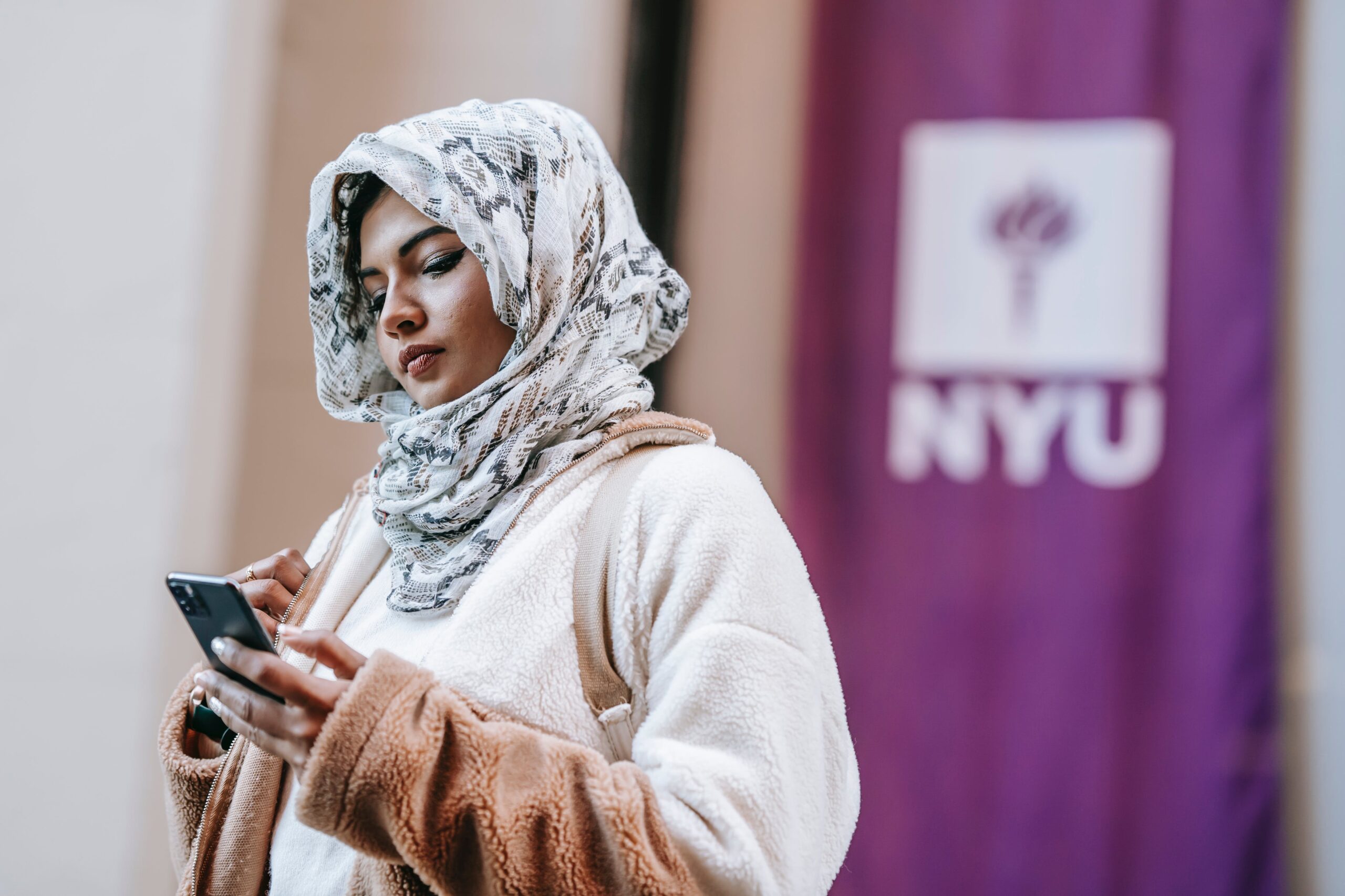 college student wearing hijab and looking at cell phone