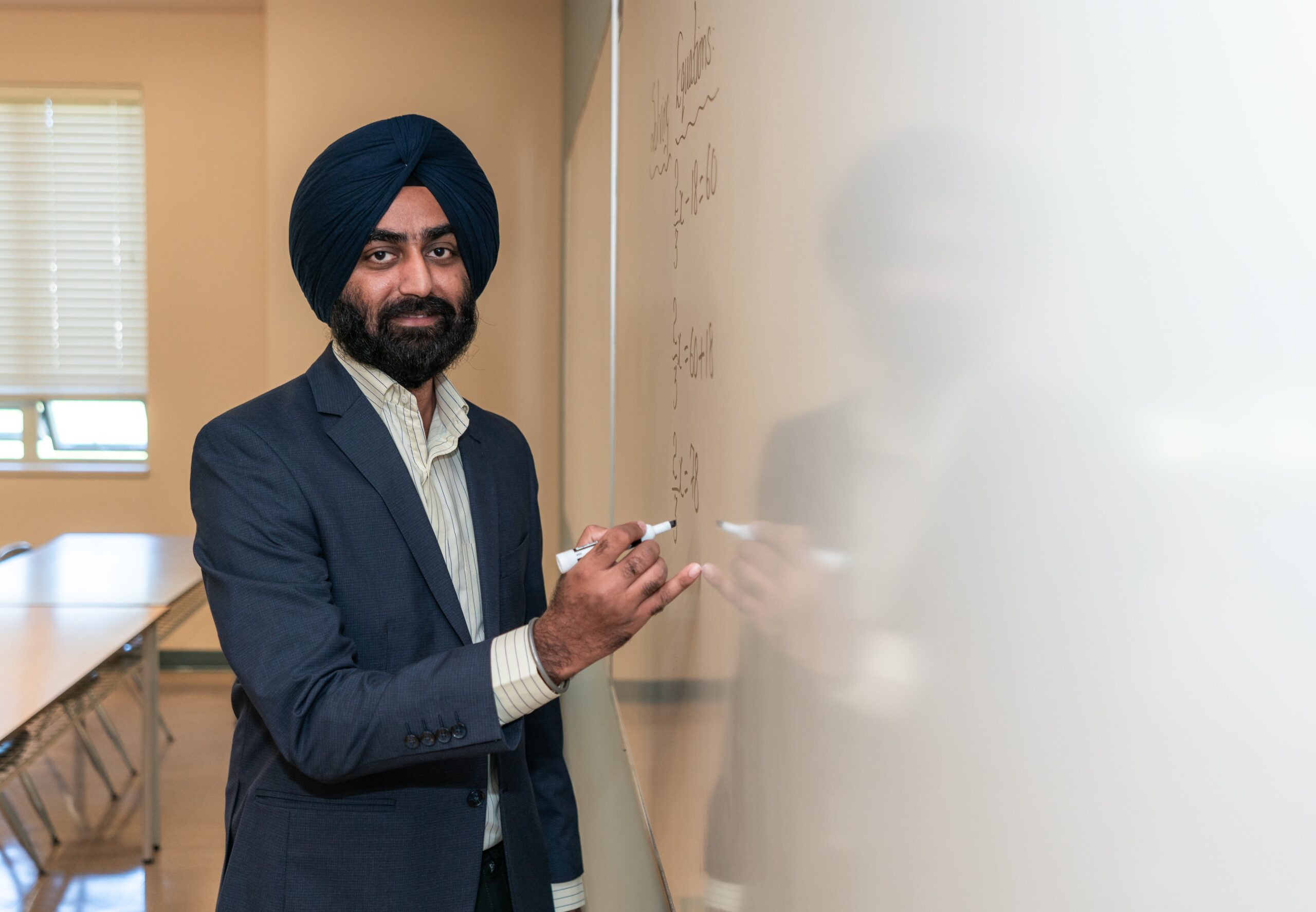 male teacher wearing a turban standing in front of a whiteboard